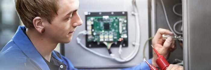 Das Foto zeigt einen jungen Mann, der mit einem Schraubenzieher an Stromkabeln arbeitet.