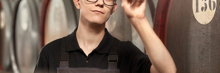 Das Foto zeigt einen jungen Mann der ein Glas mit einem Flüssigkeit vors Licht hält