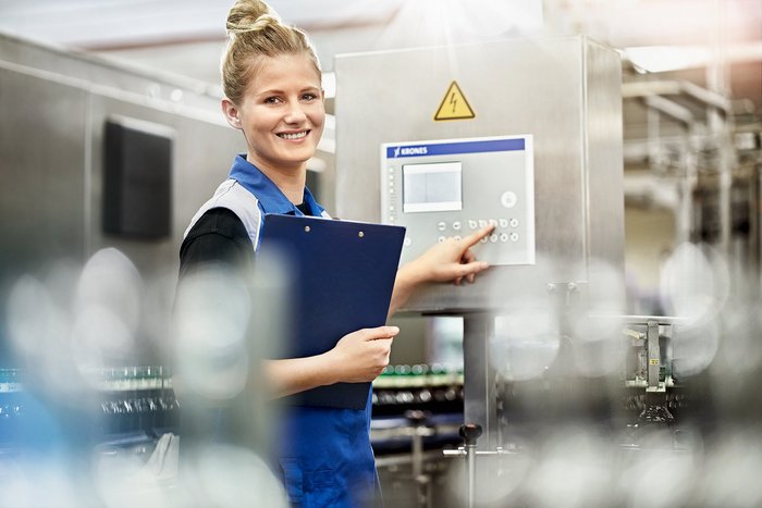 Das Foto zeigt eine junge Frau vor einem Display mit Klemmbrett in der Hand