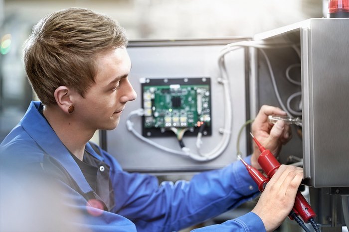 Das Foto zeigt einen jungen Mann, der mit einem Schraubenzieher an Stromkabeln arbeitet.