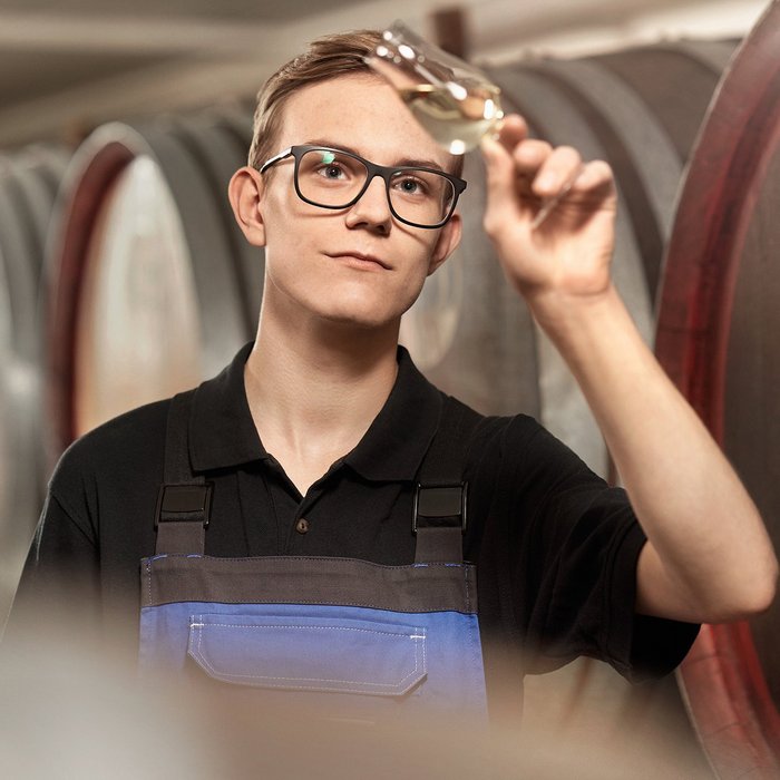 Das Foto zeigt einen jungen Mann der ein Glas mit einem Flüssigkeit vors Licht hält